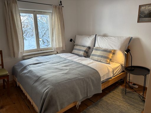 "Familienzimmer - Eltern" Gemütliches Schlafzimmer mit einem Doppelbett, Fenster und Holzstuhl.